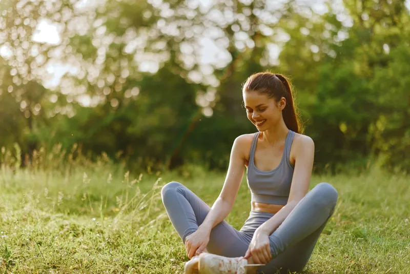 Young woman in sporty attire enjoying a sunny day outdoors, promoting a healthy lifestyle and fitness in a lush green park setting
