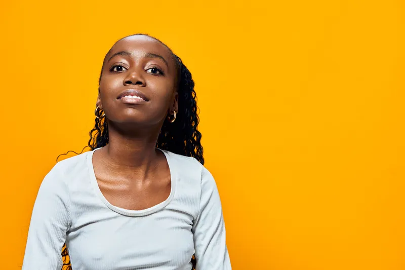 Confident young Black woman smiling on a vibrant yellow background, showcasing casual style and positive emotions in a lively, contemporary setting