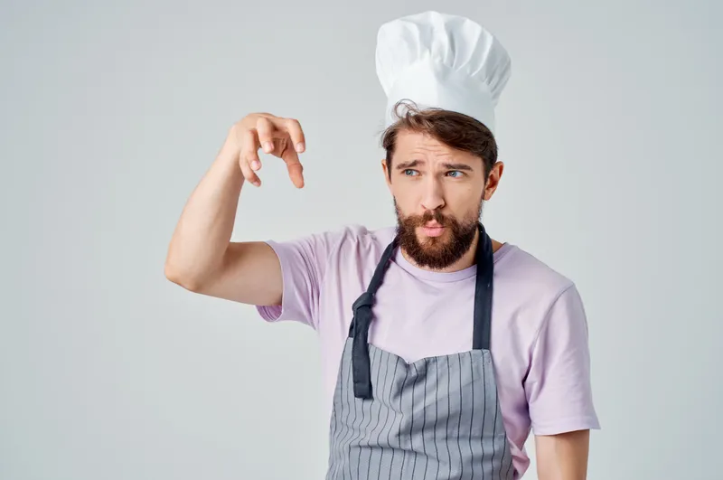 Мужчина в поварском колпаке и фартуке работает поваром на кухне ресторана