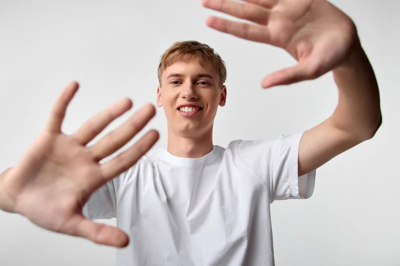 Hands, smile, young, man, framing, forward, whiteshirt, playful composition open gesture friendly mood in studio setting with bright light for casual lifestyle and youth engagement