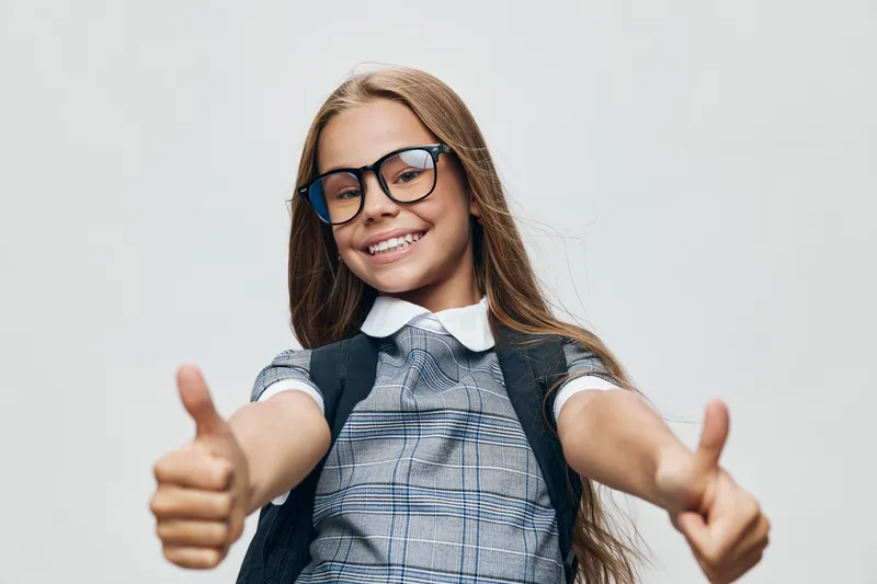 Girl smiling and showing thumbs up hand gesture for positivity happiness and confidence in casual outfit with glasses on neutral background studio portrait