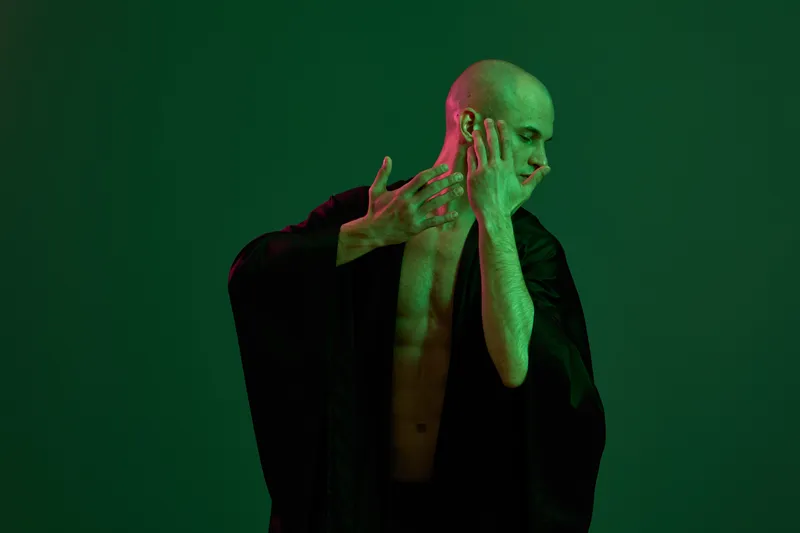 Artistic representation of a man posing dramatically, showcasing strength and emotion with a green light background for a striking contrast.