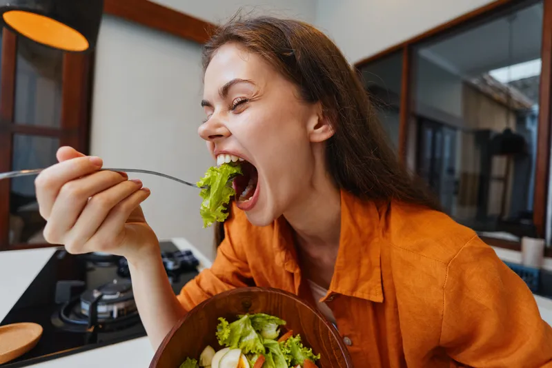 Счастливая молодая женщина наслаждается вкусным салатом на современной кухне
