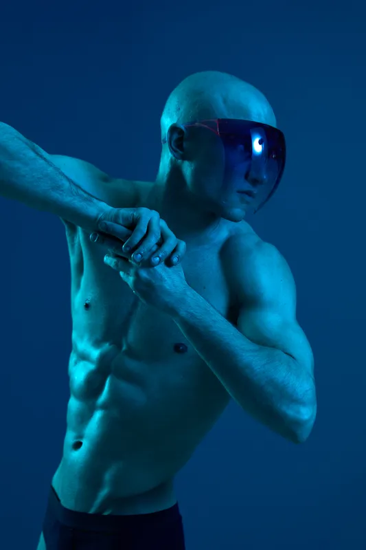 Athletic man showcasing strength in a striking blue light, wearing futuristic sunglasses. This captivating image emphasizes a sense of determination and vitality.