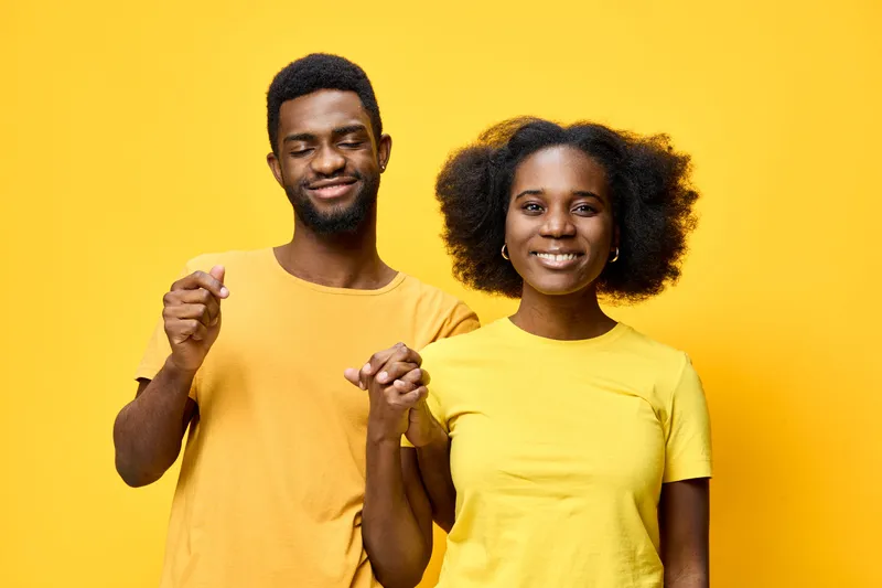 Joyful young couple in matching yellow outfits, smiling and holding hands against a bright yellow background, showcasing love and happiness