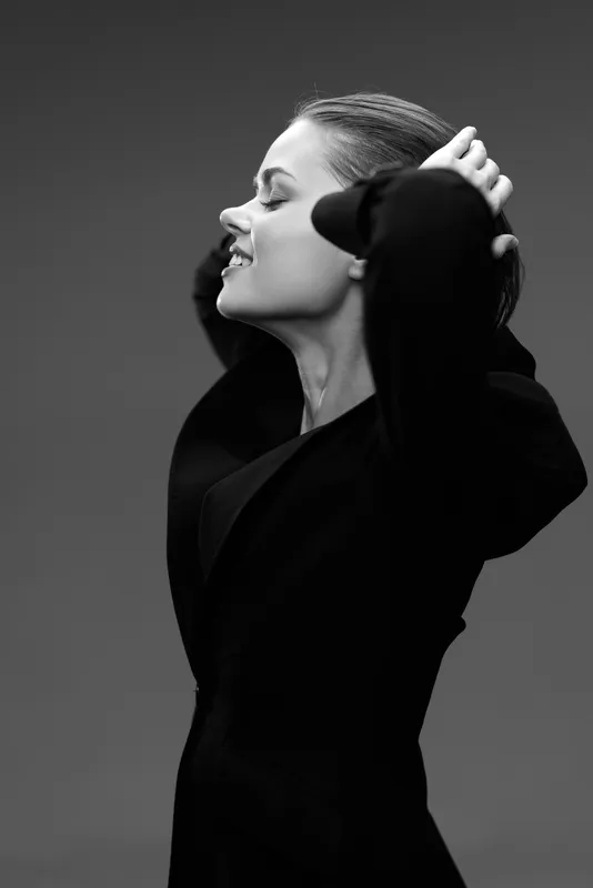 Black and white portrait of a smiling woman with closed eyes enjoying a peaceful moment in a dark jacket.