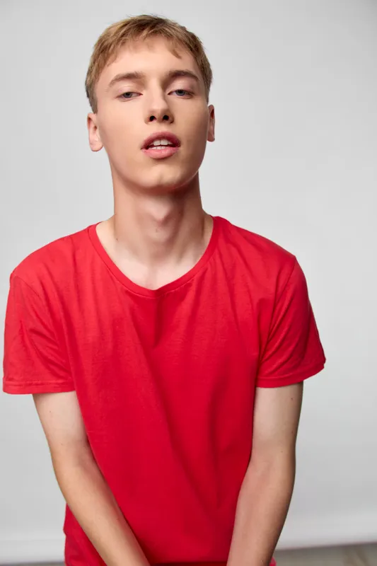 Young man in a red t shirt posing in a studio with a confident look, casual fashion, simple background, close lighting, everyday style, modern vibe