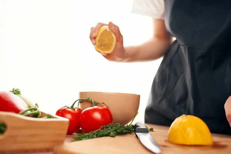 Лимон в руке на кухне, нарезка овощей для салата, приготовление еды