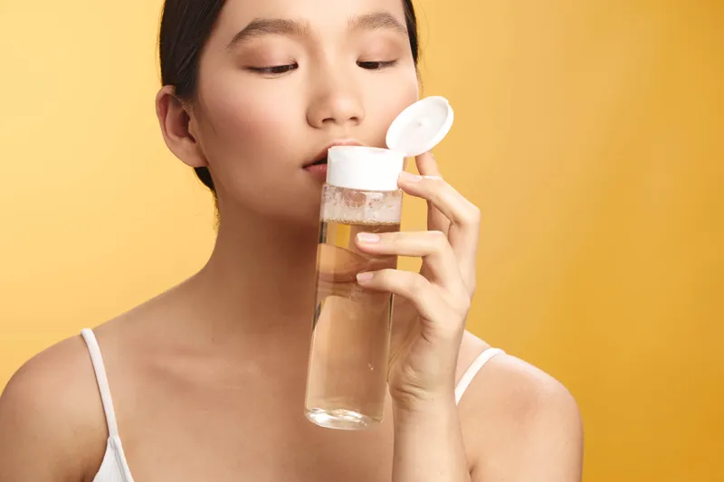 asian woman drinks water from a clear bottle in a bright studio, conveying refreshment, health, and everyday wellness with a calm, natural pose.