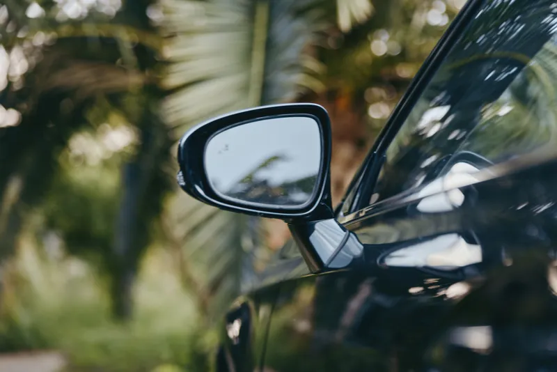 car side mirror black car tropical outdoor palm trees reflection closeup with glossy paint, adult driver unseen, casual outfit in car, travel lifestyle scene with warm golden hour atmosphere