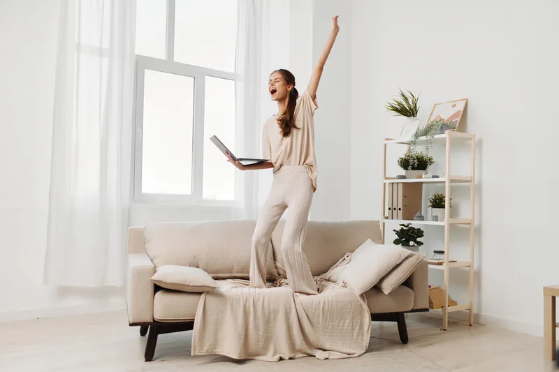 Улыбающаяся женщина работает за ноутбуком в уютной гостиной, работая из дома