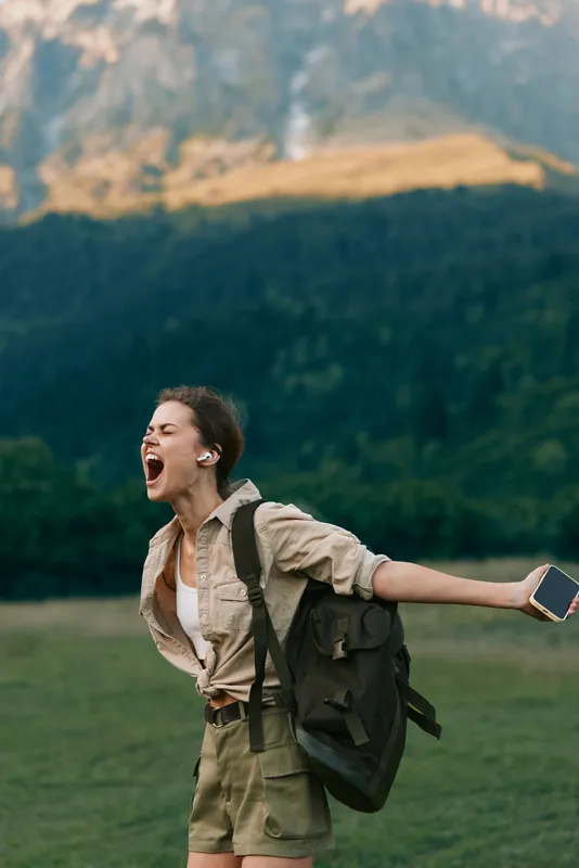Energetic woman outdoors with a backpack, shouting joyfully in a green field, capturing a hiking mood and travel vibe, nature escape, spontaneous moment, carefree energy.
