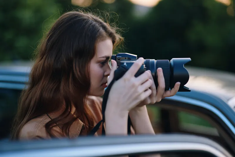 Young female photographer capturing moments outdoors with a DSLR camera, showcasing a passion for photography in a natural setting.