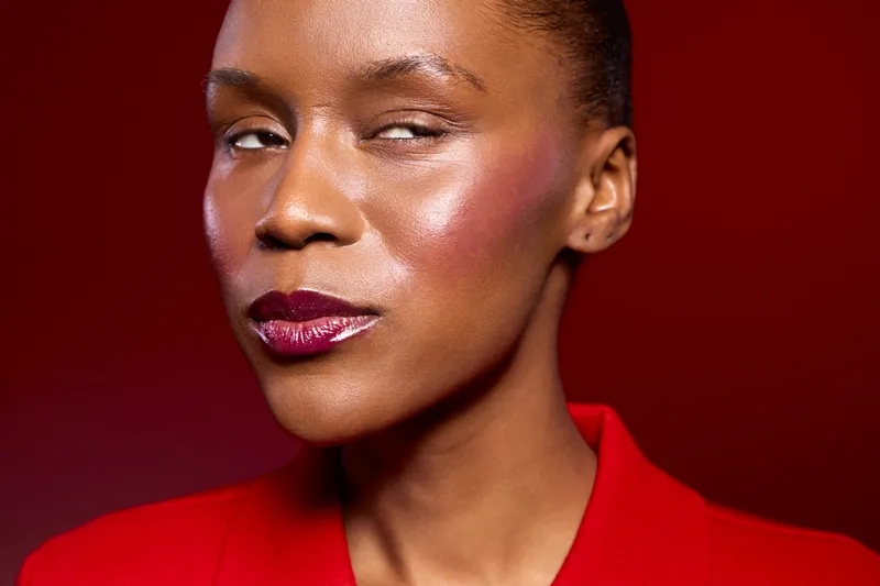 Close-up portrait of confident black woman with dark skin wearing red jacket on red background. Concept of beauty, fashion, elegance, and strong female expression in studio lighting.