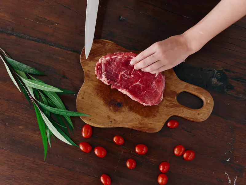 Женщина с ножом в руке нарезает свежее стейковое мясо для жарки на кухне