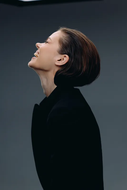 Profile of a smiling woman with short hair wearing a black outfit against a dark background, expressing joy and confidence.