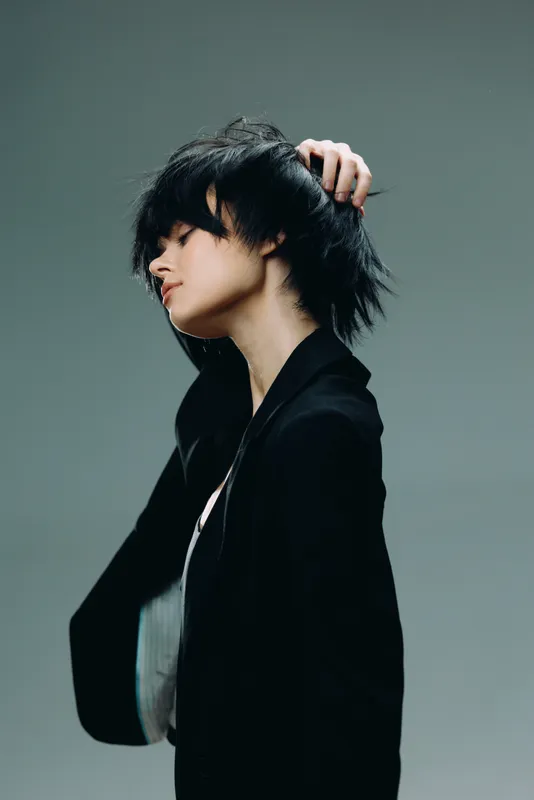 Stylish woman with short black hair in a black blazer posing thoughtfully against gray background