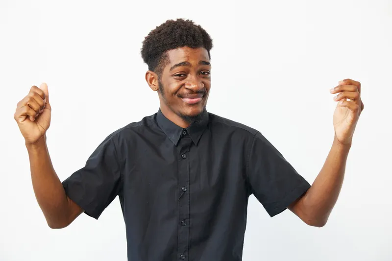 A smiling Black man expresses joy and enthusiasm, wearing a stylish black shirt against a clean white background. Perfect for lifestyle or celebration themes.
