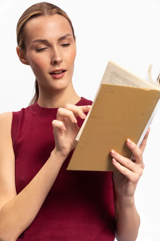 Young woman in red sleeveless top reading a book with focus and curiosity. Isolated on white background. Concept for education, knowledge, learning, and concentration.