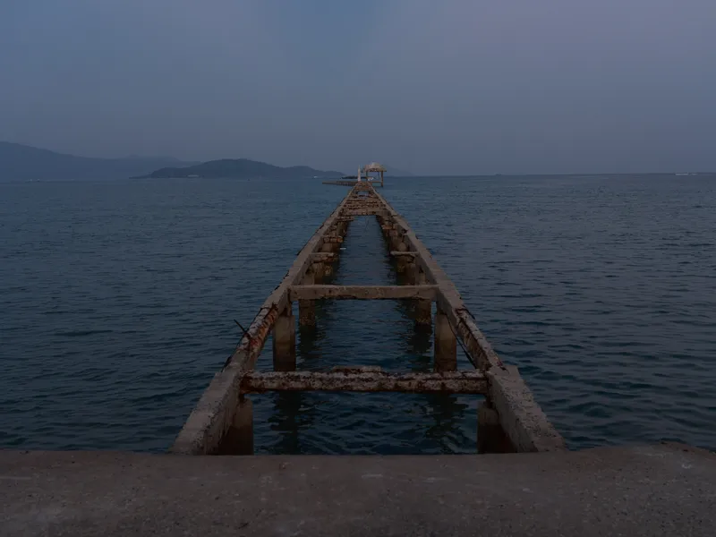 abandoned pier extending into calm sea under dusk sky with distant islands and tranquil atmosphere