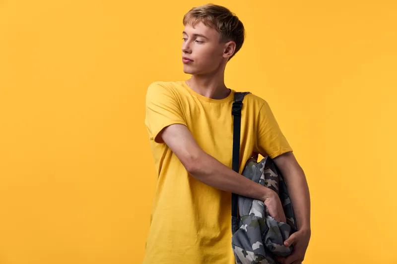Young student wearing a yellow tee with a camouflage backpack against a vibrant yellow backdrop, casual urban style ready for class or travel and everyday adventures