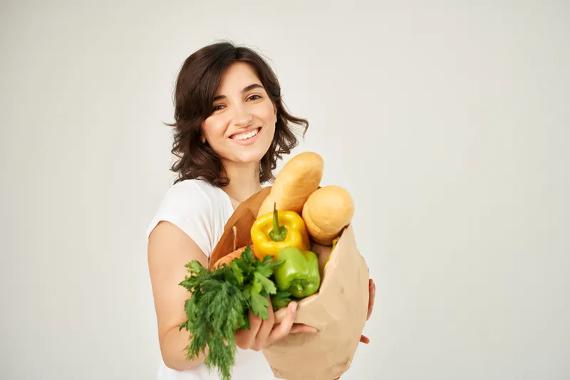 Весёлая брюнетка с продуктами, овощами на светлом фоне