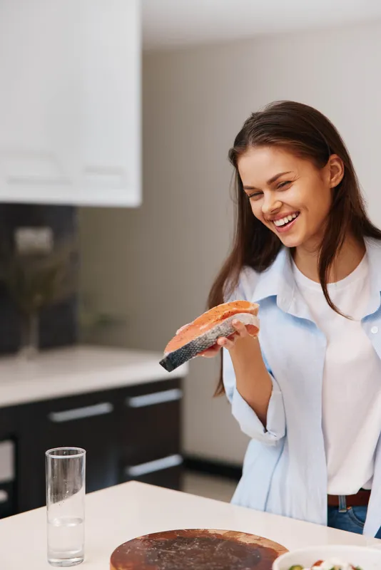 Женщина держит кусок лосося на кухне, готовя здоровое блюдо из морепродуктов на ужин