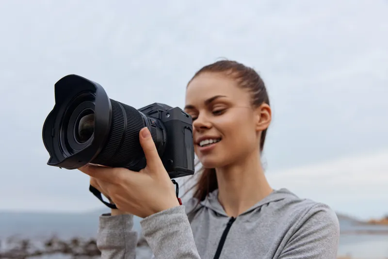 Young woman enthusiastically photographing with a DSLR camera by the sea, showcasing passion for photography and the joy of capturing moments