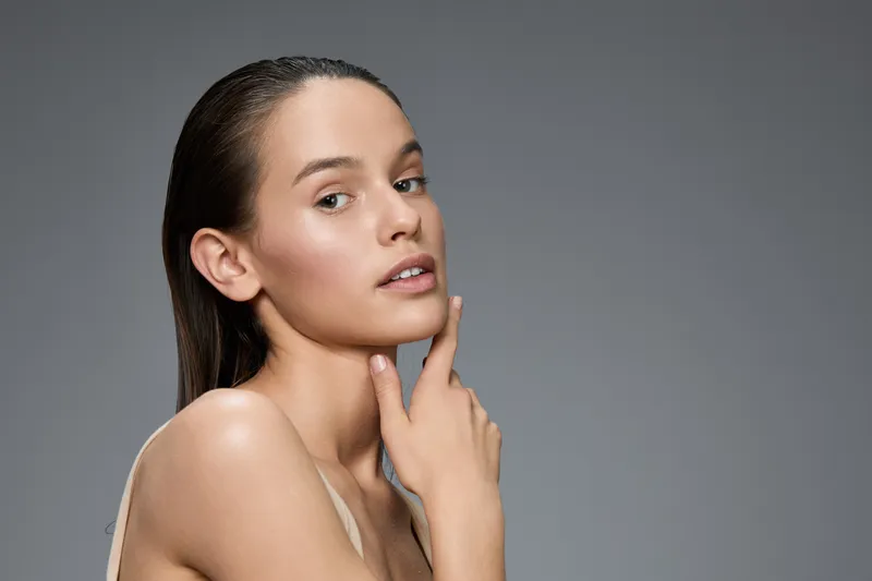 Beautiful young woman with clear skin and wet hair posing gracefully against a gray background, showcasing natural beauty and confidence