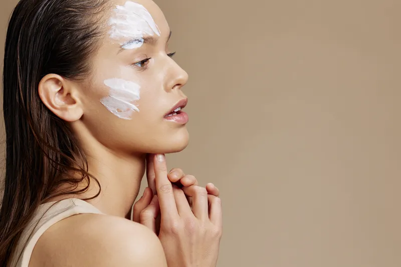 Брюнетка держит руку возле лица с кремом, что передает идею омоложения и очарования