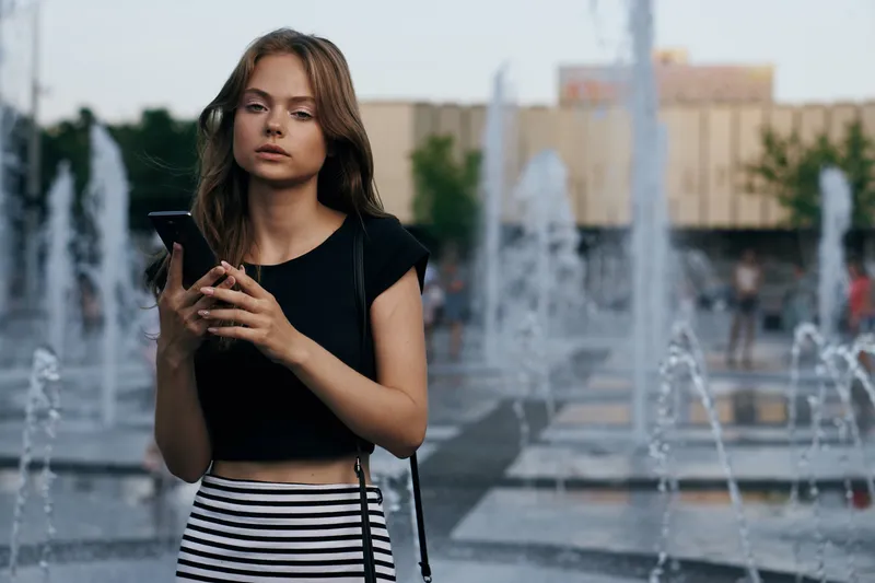 Женщина у фонтана на улице в черной футболке, обрезанный вид, распущенные волосы, красивая модель