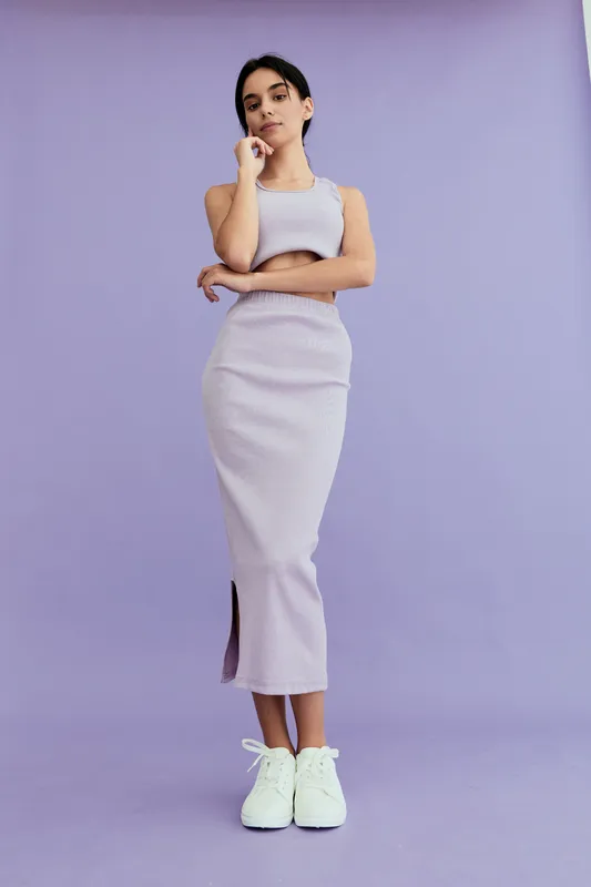 young woman in lilac striped dress posing confidently against purple background, wearing white sneakers with thoughtful expression and crossed arms