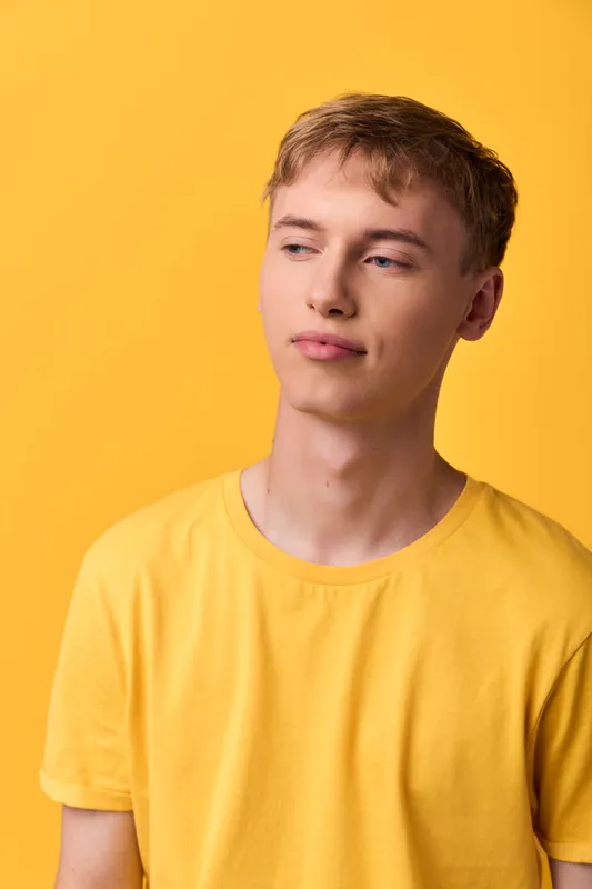 Young male in a yellow shirt stands against a matching yellow backdrop, conveying casual confidence and relaxed mood for lifestyle, fashion, or studio concepts and marketing visuals