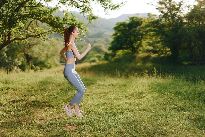 Young woman in athletic wear jogging outdoors in a sunny park, showcasing fitness and vitality, surrounded by lush greenery and a bright sky