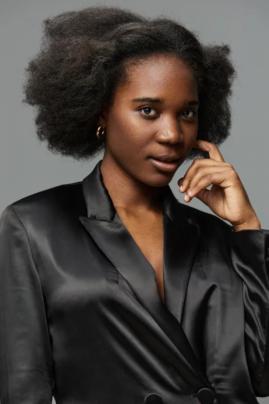 Elegant young woman with natural afro hairstyle in a stylish black blazer, exuding confidence and poise against a grey background
