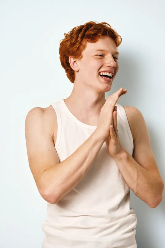 Young man with red hair wearing sleeveless shirt smiling and clapping hands. Portrait of happy male with fair skin and freckles on white background for lifestyle.