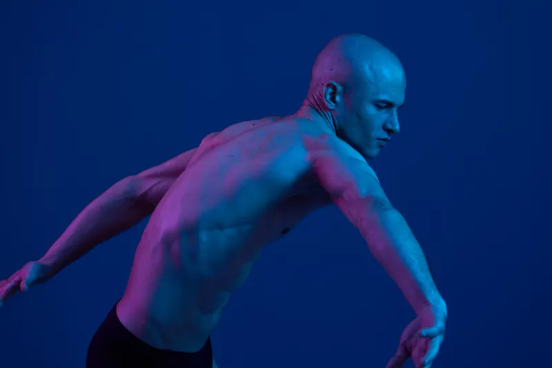 Athletic man in dynamic pose, showcasing strength and movement against a blue background with vibrant lighting. Unique composition enhances energy and creativity.