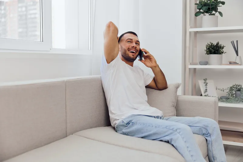 Happy man talking on the phone, embracing emotional connection and vulnerability, representing modern challenges and self-care in personal spaces.