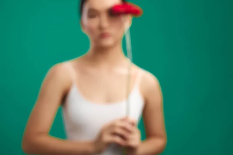 asian woman stands before a vibrant backdrop with a soft blur, holding a flower near her chest, conveying a calm, contemplative mood and subtle studio lighting that highlights gentle mood.