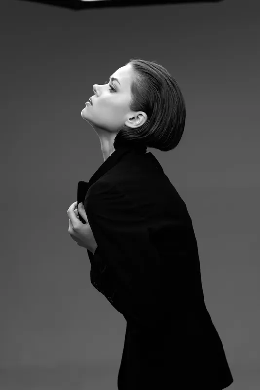 Black and white profile of a woman in a dark coat expressing emotion and elegance in a studio setting