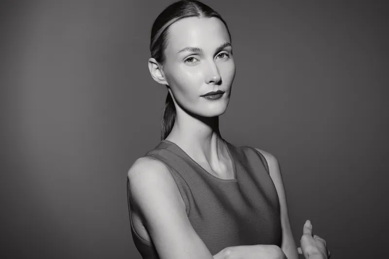 Young caucasian woman with pale skin and tied hair poses confidently in sleeveless top on grey background studio.
