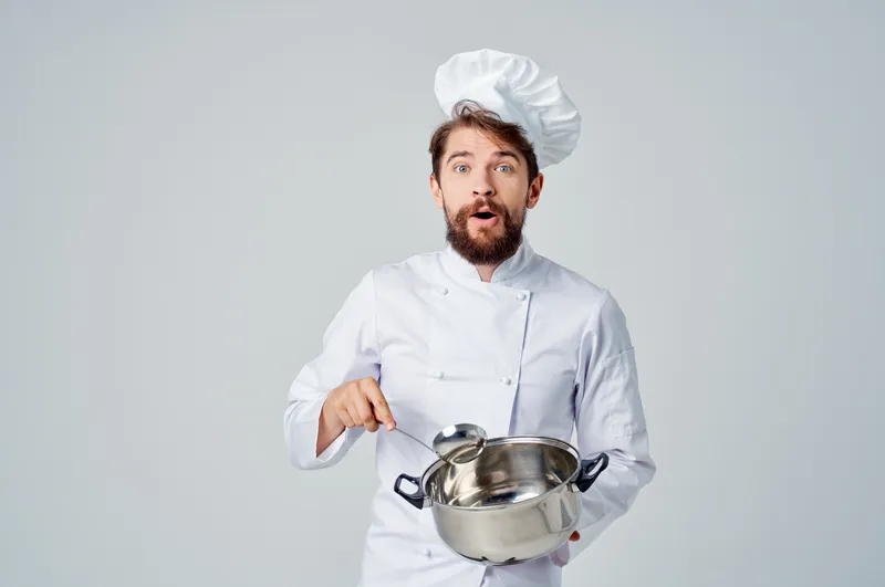 Повар готовит еду в кастрюле на кухне, занимаясь кулинарной работой