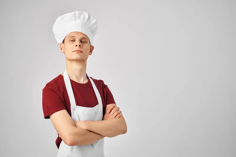 Мужчина в белом фартуке и кепке на голове в рабочей униформе на кухне
