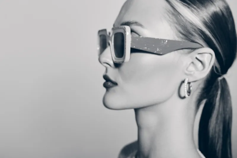 Profile of a fair skinned white woman wearing stylish sunglasses and hoop earrings with tied back hair. Concept for fashion, summer style, and beauty portrait in monochrome.