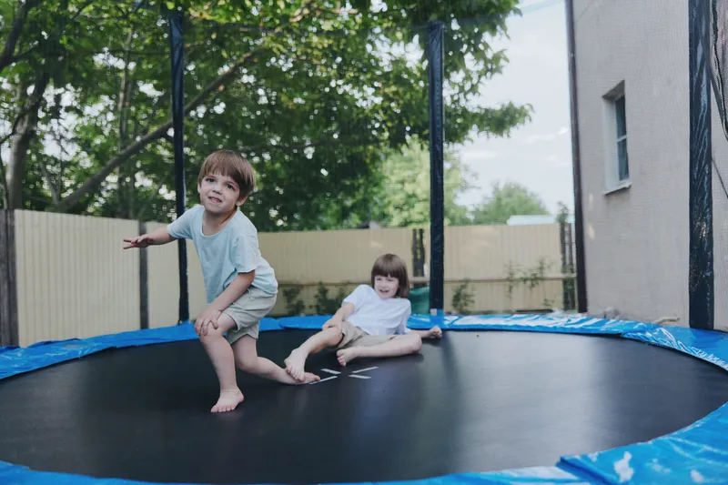 Laughing children playing on a trampoline, enjoying the sunny day outdoors surrounded by trees and bright blue sky, showcasing joy and freedom.