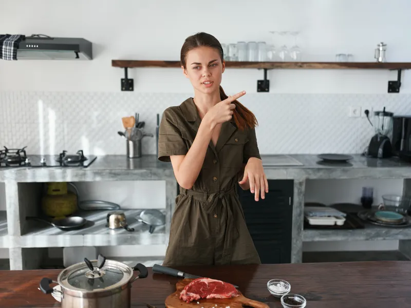 Уставшая женщина дома на кухне готовит еду, используя мясо и овощи