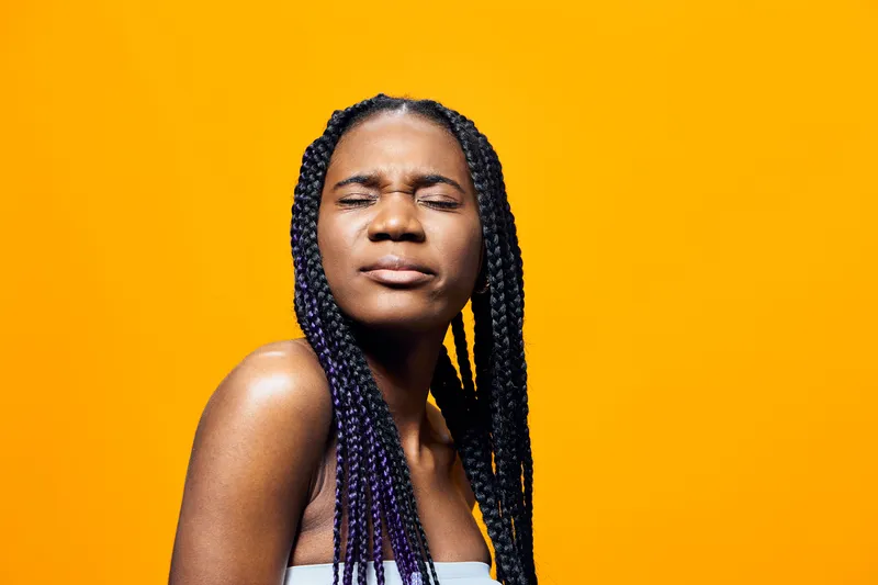Portrait of an African girl with braided hair against a bright yellow background, conveying confidence and joy, suitable for youth culture and beauty concepts