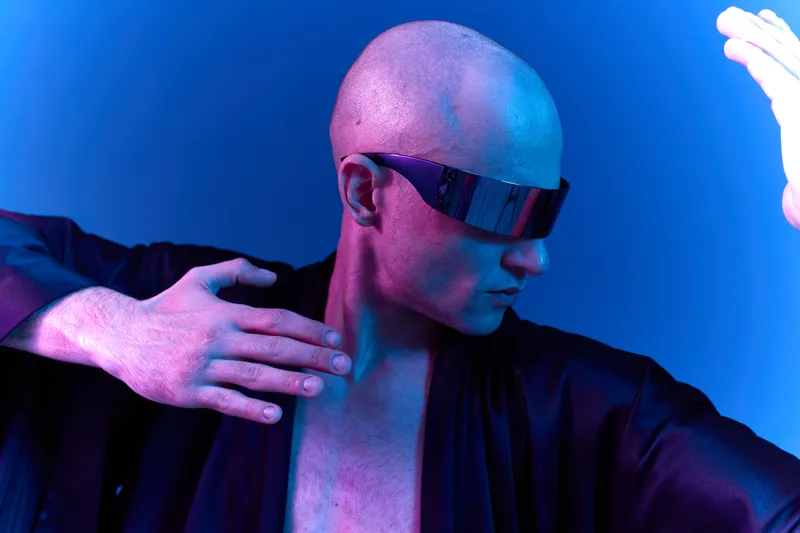 Futuristic man in stylish sunglasses striking a dynamic pose, bathed in vibrant blue and purple light, showcasing an artistic blend of colors and energy.