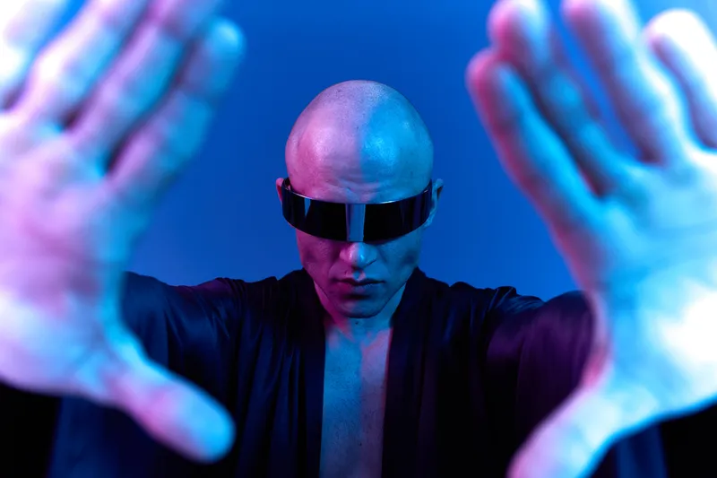 Futuristic man wearing sunglasses, creating a striking visual with his hands outstretched, immersed in blue light and modern aesthetics, exuding strength and confidence.
