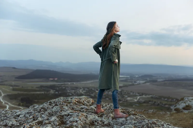 Женщина любуется захватывающей панорамой с вершины горы, на заднем плане виднеются долина и горы